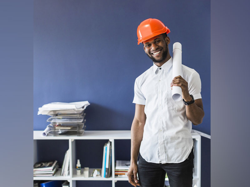 Young African black engineer smiling wearing hardhat holding rolledup blueprint Free Photo