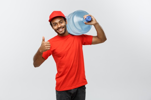 Delivery concept - handsome african american delivery man holding water tank. isolated on grey studio background. copy space. Free Photo