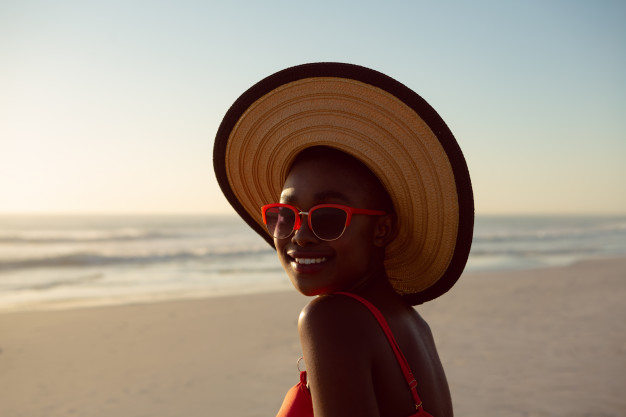 African black Woman in hat and sunglasses relaxing on the beach – Free Photo