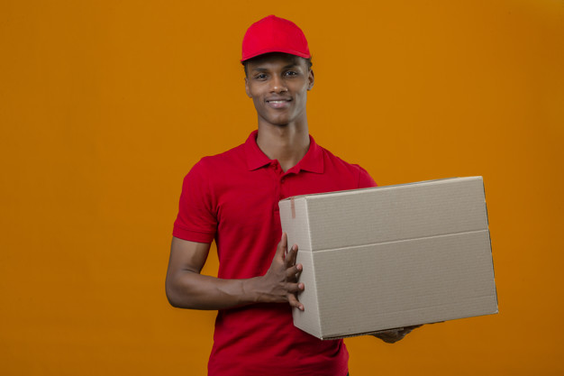 Young african american delivery man wearing red polo shirt and cap holding box package with smile on face over isolated orange Free Photo