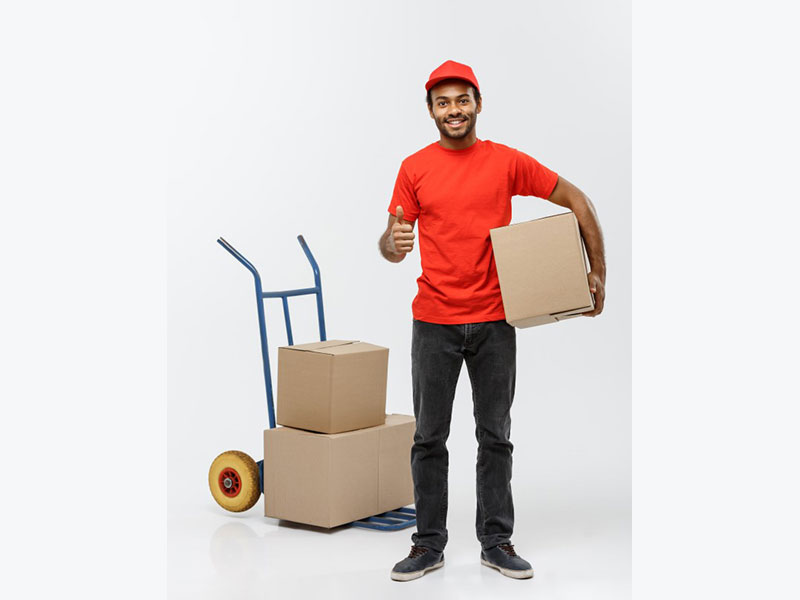 Delivery concept - portrait of handsome african american delivery man or courier pushing hand truck with stack of boxes. isolated on grey studio background. copy space. Free Photo