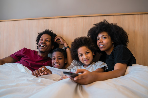 Family watching a movie on bed at home. Free Photo