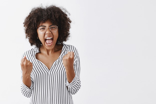 Pissed annoyed African American black female office manager in striped blouse and glasses clenching fists with angry emotions yelling and showing being sick and tired of stupid coworker Free Photo