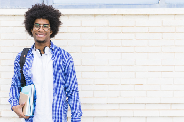 Portrait of smiling afro american male student standing against white brick wall Free Photo
