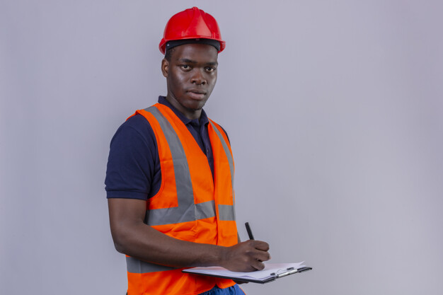 Young african american builder man wearing construction vest and safety helmet holding clipboard and pen with serious face standing Free Photo