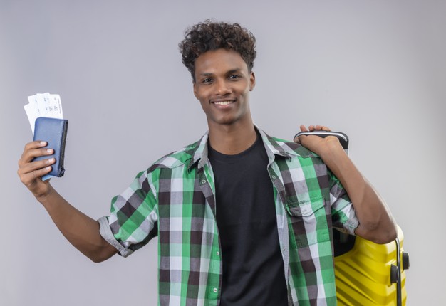 Young african american traveler man standing with suitcase holding air tickets smiling cheerfully positive and happy over white background Free Photo