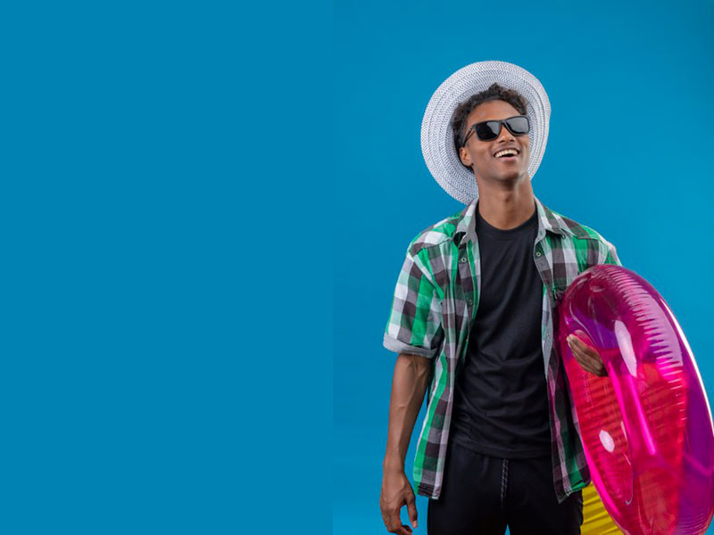 Young african american traveler man in summer hat wearing black sunglasses holding inflatable ring smiling cheerfully happy and positive standing over blue background Free Photo