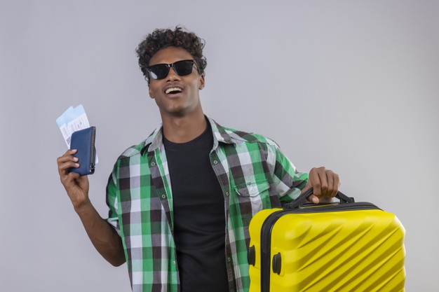 Young african american traveler man wearing black sunglasses standing with suitcase holding air tickets smiling cheerfully positive and happy over white background Free Photo