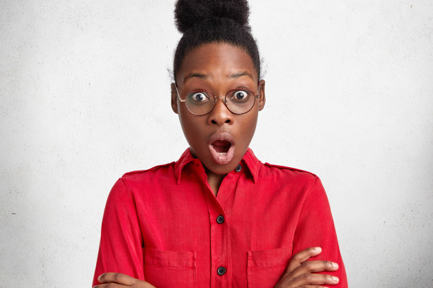 Beautiful emotional dark skinned businesswoman wears red formal blouse and spectacles, stares at camera with shocked expression, has deadline to prepare business project. omg and ethnicity concept Free Photo