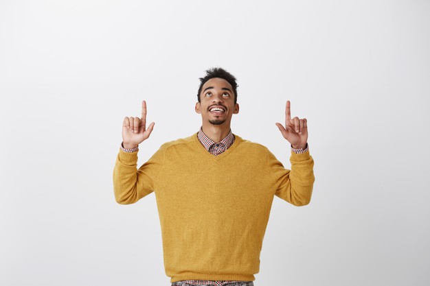 Thanks god it is friday. portrait of pleased interested young african-american student in stylish yellow sweater raising hands, looking and pointing up, enjoying nice view of sky Free Photo