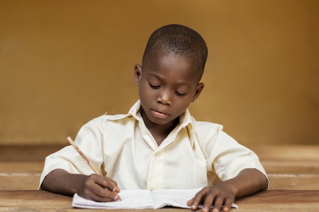 African Black Boy Learning In Class Room Writing In Book With Pencil