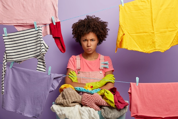 Unhappy African black woman arms folded washing clothes - Cariblens