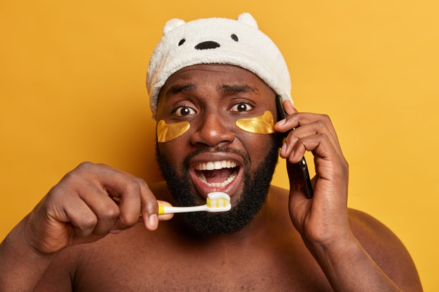 African black man brushing teeth – wears collagen patches under eyes