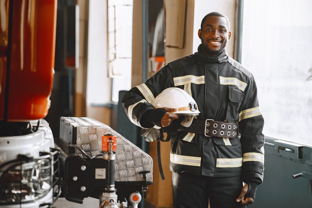 African black firefighter standing in front of a fire engine Free Photo