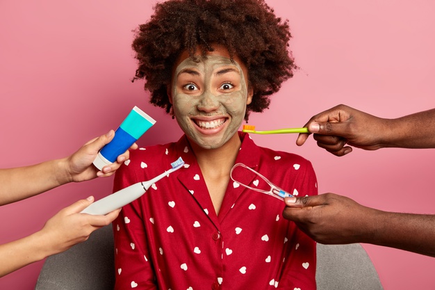 Young African black woman applies clay mask – dental care surrounded by hands with toothbrushes