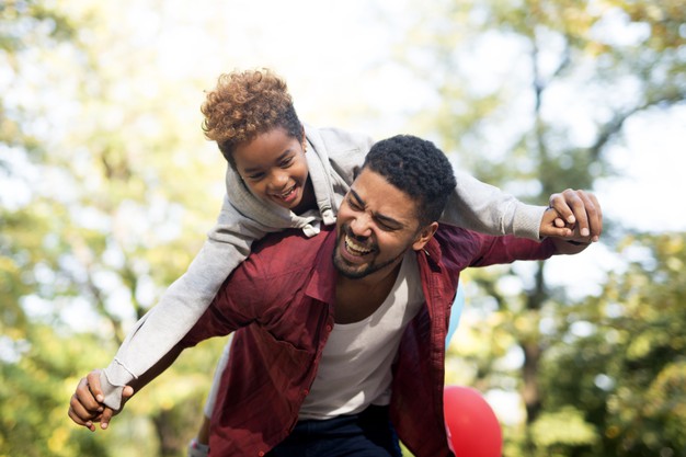 African black Father carrying daughter on his back with arms spread