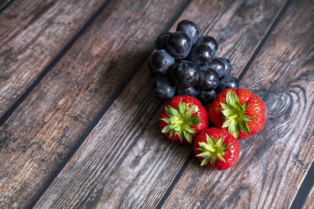 Fresh scottish strawberries and black grapes on top of wooden table. Free Photo