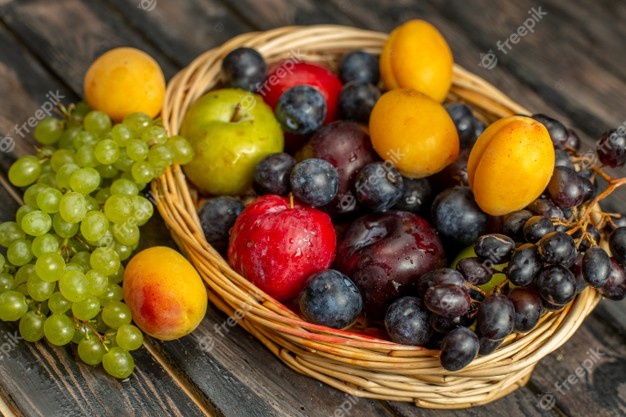 Half-top view basket with fruits mellow and sour fruits such as grapes apricots plums on the brown desk Free Photo