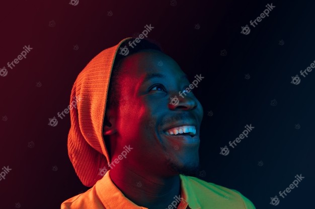 Close up portrait of a happy young african american man smiling against black neon studio background Free Photo