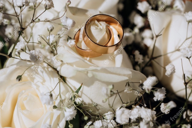Golden wedding rings on the white rose from the wedding bouquet Free Photo