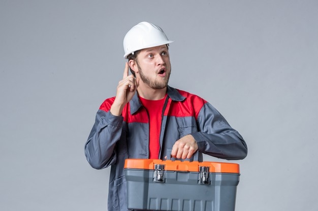 Front view male builder in uniform and helmet holding tool case on gray background Free Photo