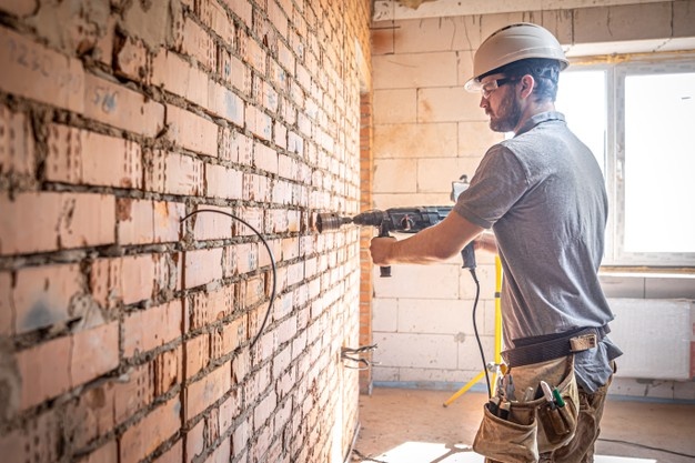 Handyman at a construction site in the process of drilling a wall with a perforator. Free Photo