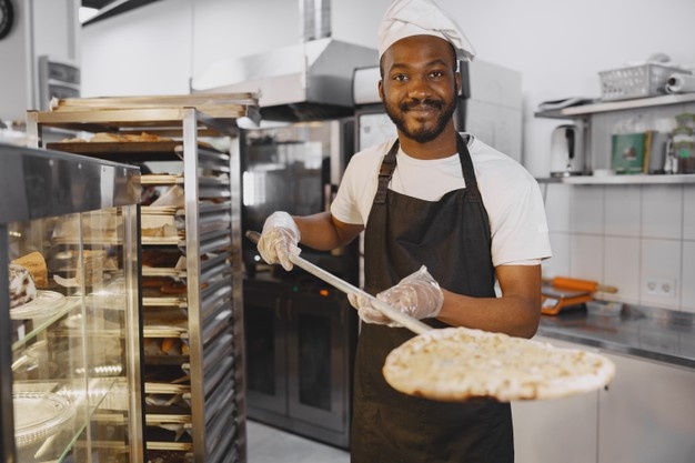 Handsome pizzaiolo making pizza at kitchen in pizzeria. african american ethnicity. Free Photo