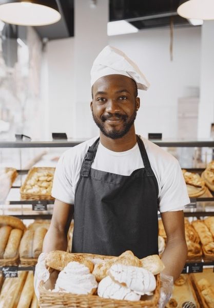 Portrait of african-american baker with fresh bread at the bakery. pastry chef holding small pastry. Free Photo