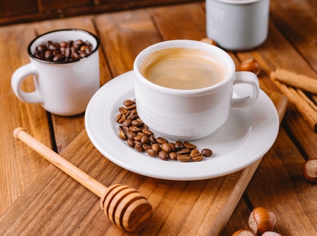 Close up of coffee cup decorated with coffee beans placed on wooden serving board Free Photo