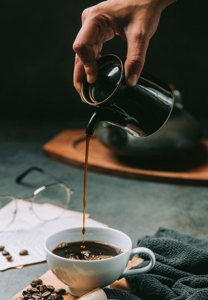 A close-up of a hand pouring coffee water into a coffee cup, international coffee day concept Free Photo