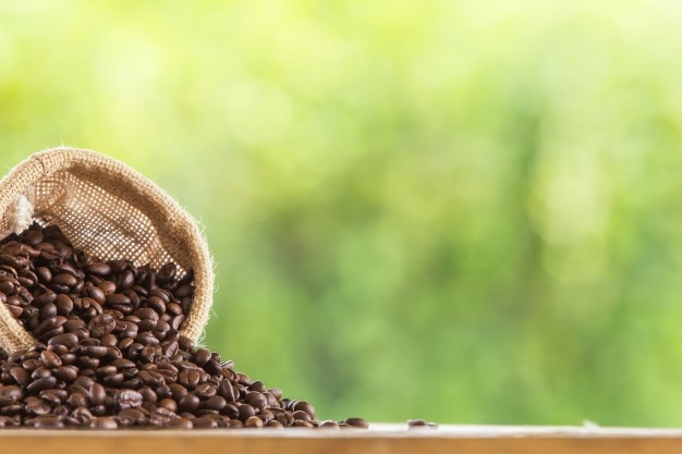 Coffee bean in sack on wooden tabletop against grunge green blur background Free Photo