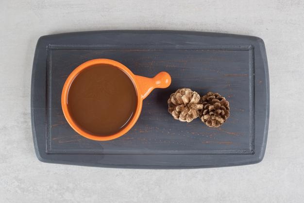 Cup of coffee and pinecones on dark plate Free Photo