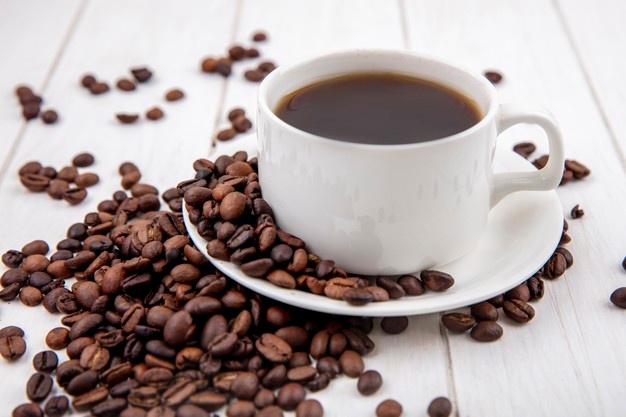 Side view of coffee on a white cup with coffee beans isolated on a white wooden background Free Photo