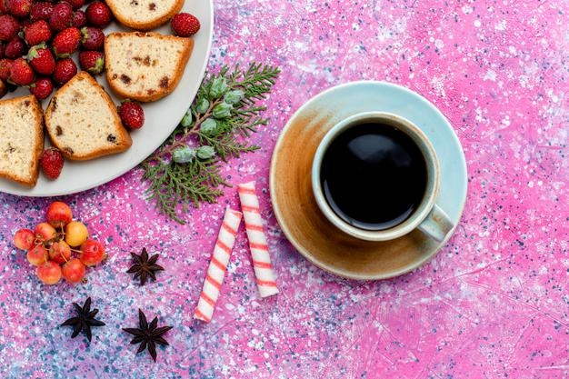 Top view sliced yummy cakes with fresh red strawberries and cup of coffee on pink desk Free Photo