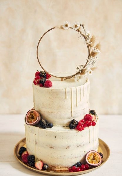 Vertical shot of a wedding cake decorated with fresh fruits and berries and a flower ring Free Photo