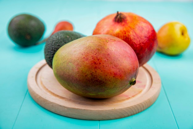 Front view of mango with pomegranate on a wooden kitchen board on blue surface Free Photo