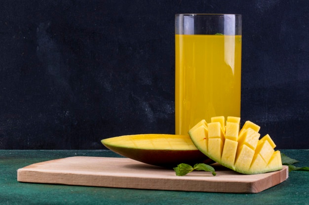 Front view sliced mango on blackboard with a glass of orange juice and mint leaves Free Photo