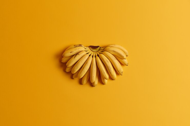 Bunch of small ripe baby bananas contain essential nutrients for health isolated on yellow background. summer fruits concept. flat lay, top view. natural vitamin source. diet and healthy food Free Photo