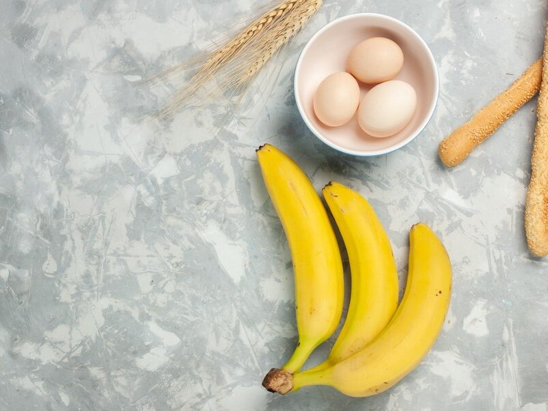 Top view yellow bananas with raw eggs and bun bread on light-white desk Free Photo