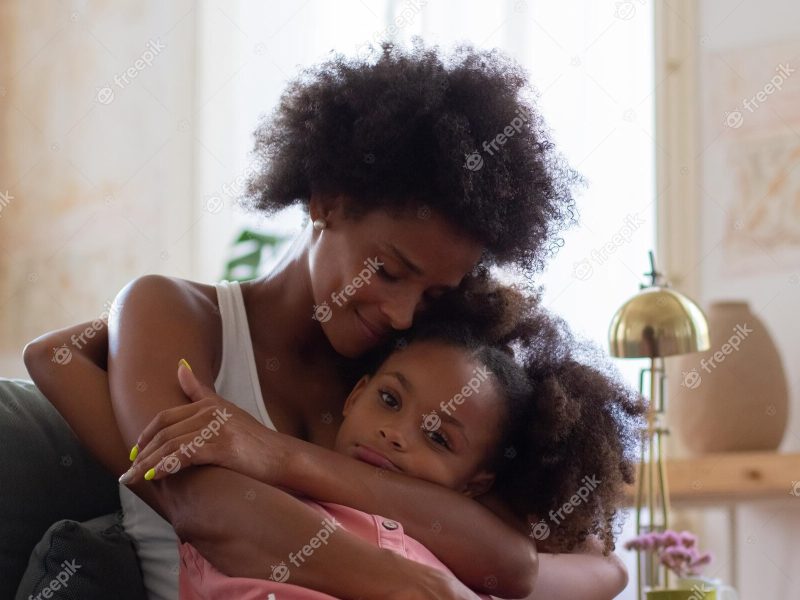 African American black mother and daughter hugging lovingly on the couch