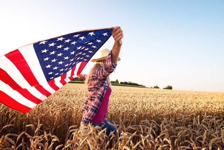 Attractive blonde female walking through wheat field and holding usa waving flag Free Photo