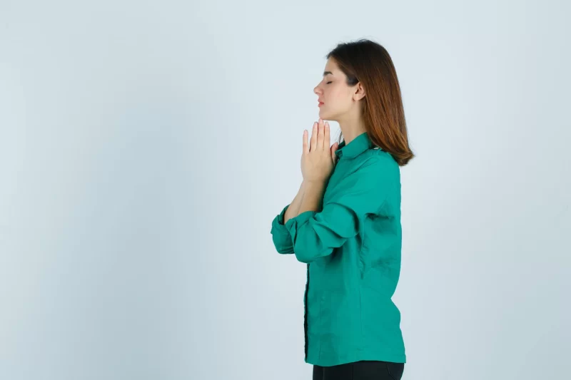 Beautiful young lady holding hands in praying gesture in green shirt and looking hopeful. . Free Photo