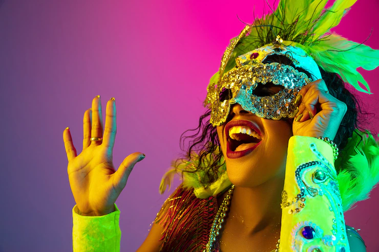 Beautiful young woman in carnival, stylish masquerade costume with feathers on gradient wall in neon light Free Photo