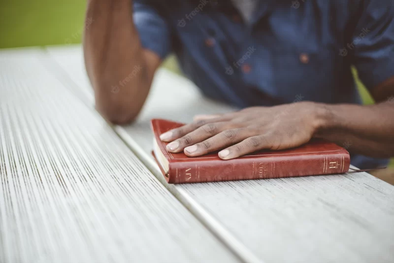 Closeup shot of a male with his hand on the bible on a wooden table Free Photo