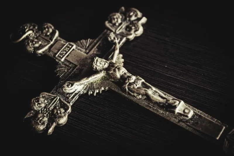 Closeup shot of a metal cross on a wooden black table Free Photo