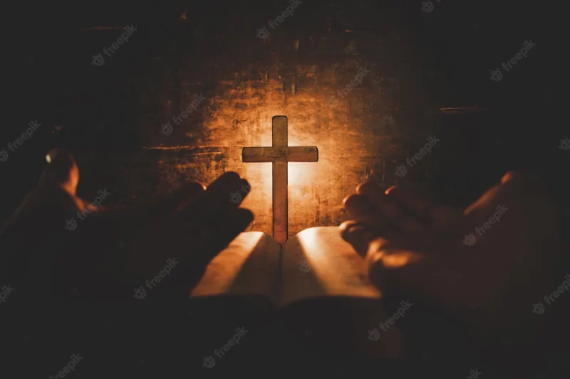 Conceptual image focus on candle light with man hand holding wooden cross on bible and blurred w