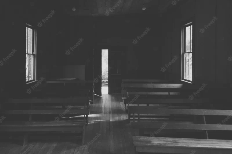 An interior of a small church in the countryside with wooden benches and an opened door Free Photo