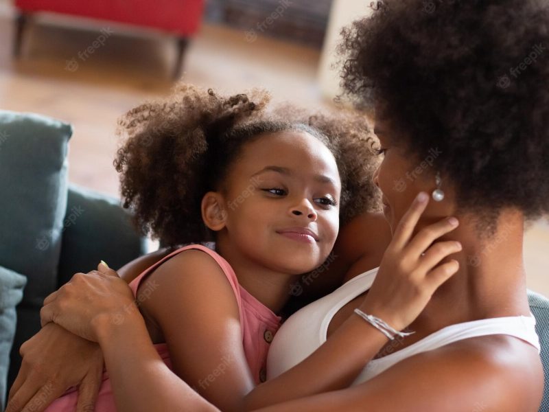 Loving black African American mother and daughter hugging on couch