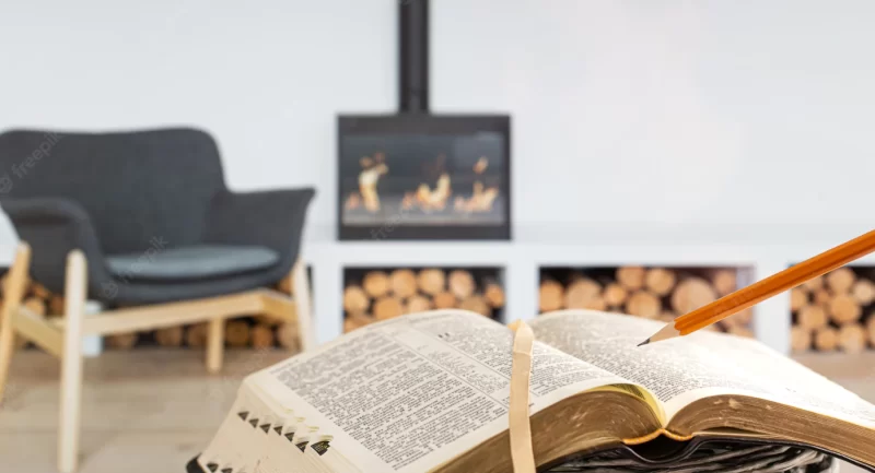 A man holding a bible with a pencil, against the background of the living room with a fireplace. readi