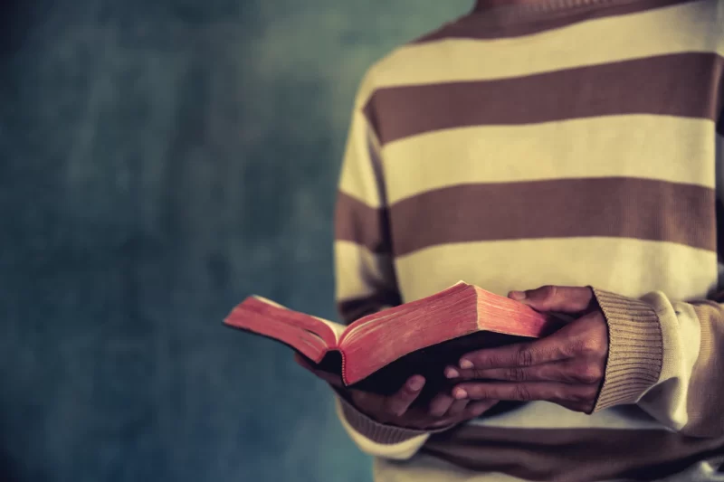 A man standing while reading bible or book over concrete wall with window light Free Photo